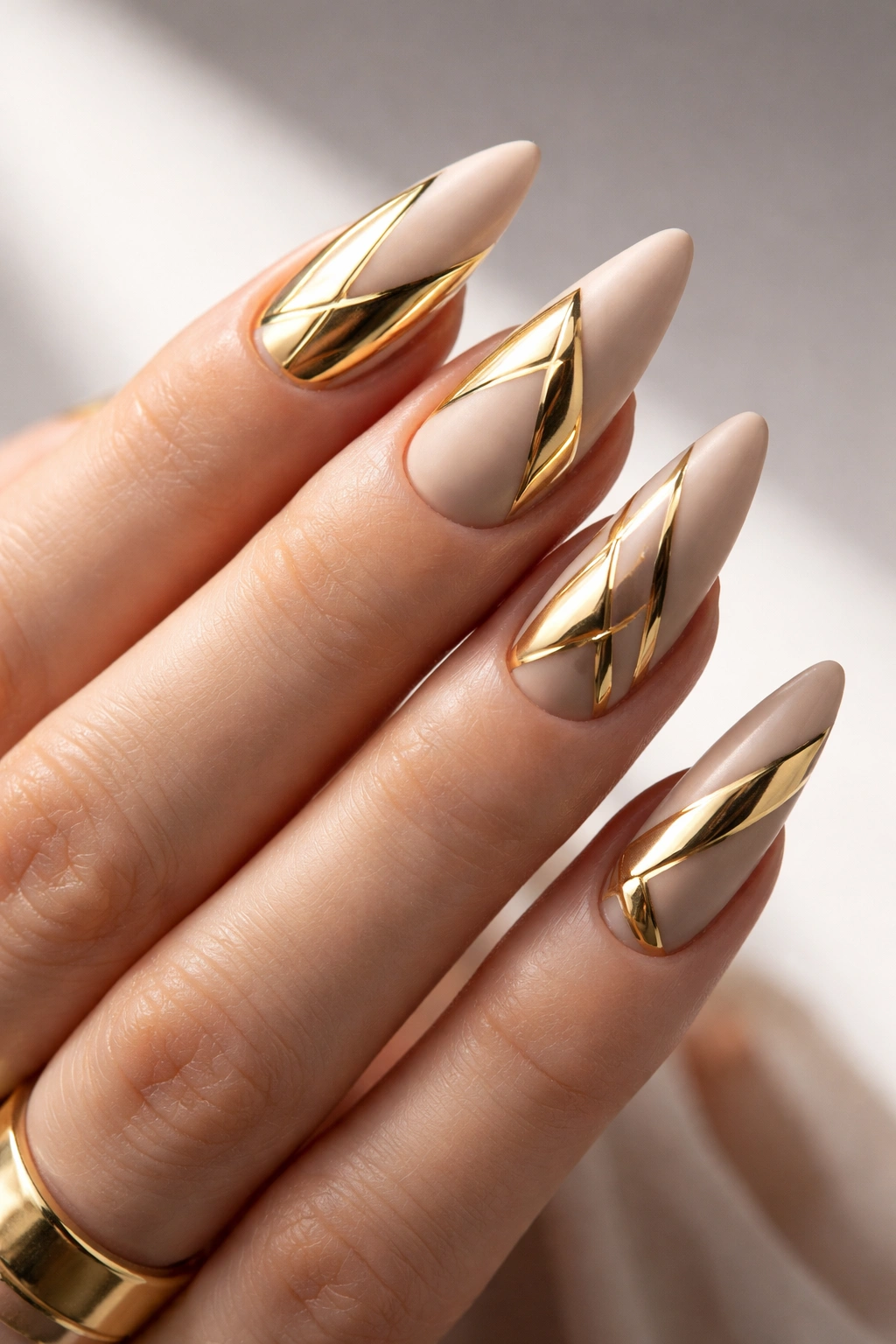 Close-up of nude matte nails with geometric gold chrome shapes