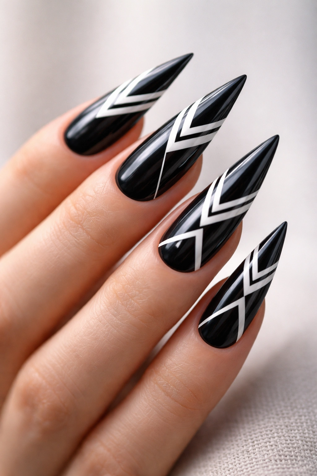 Close-up of stiletto nails with black base and white geometric patterns on a bare hand