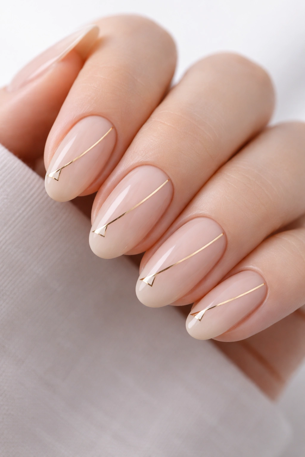 Close-up of nude nails with slim gold line and small triangle accents