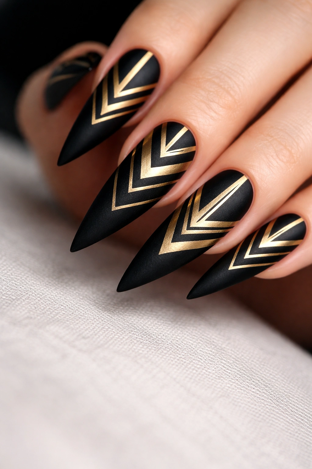Matte black stiletto nail with geometric gold pattern