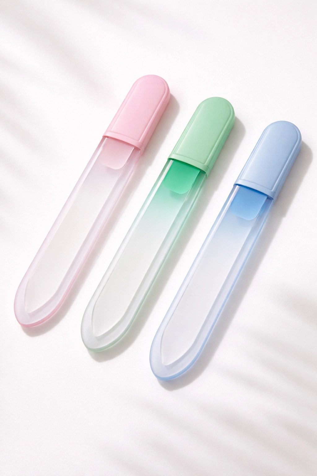 Three crystal glass nail files with colored cases on white surface