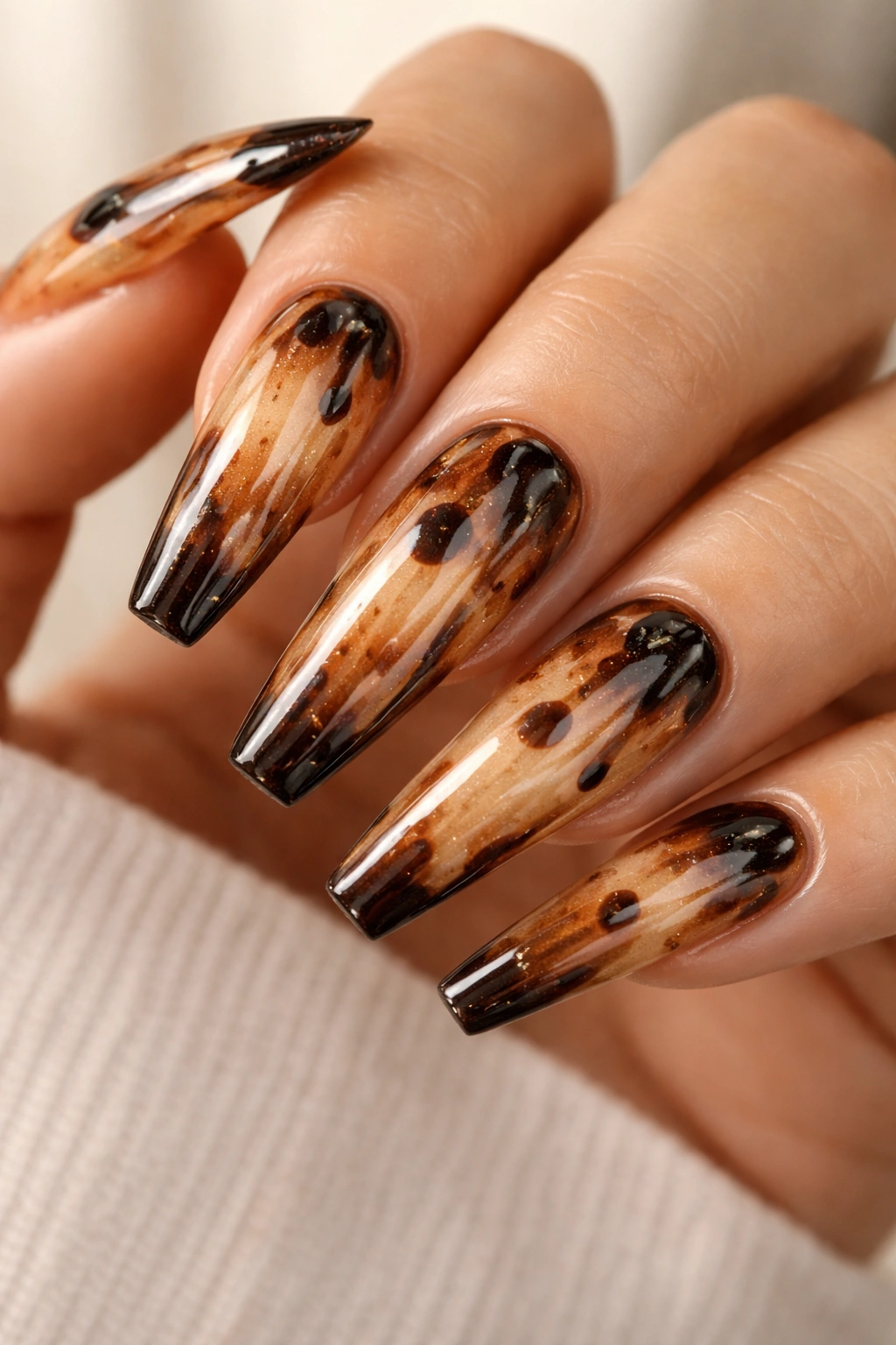 Close-up of coffin nails with caramel glaze and dark accents on a neutral background