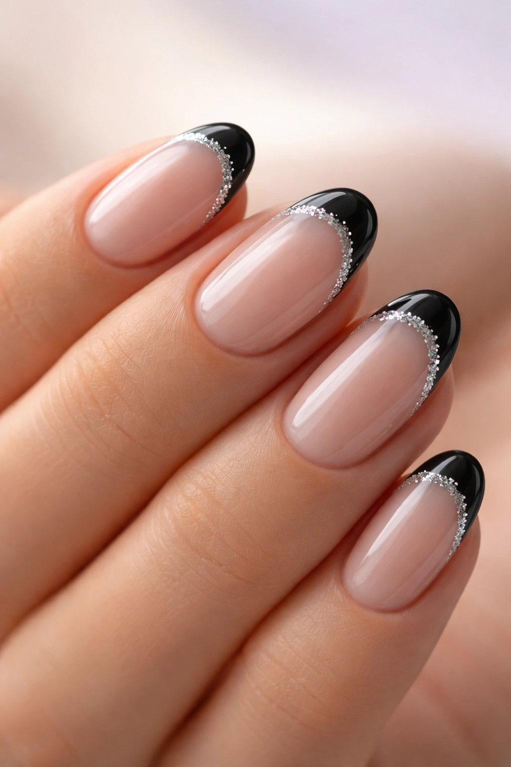 Close-up of short oval nails with glitter-edged black tips and a subtle shimmer.