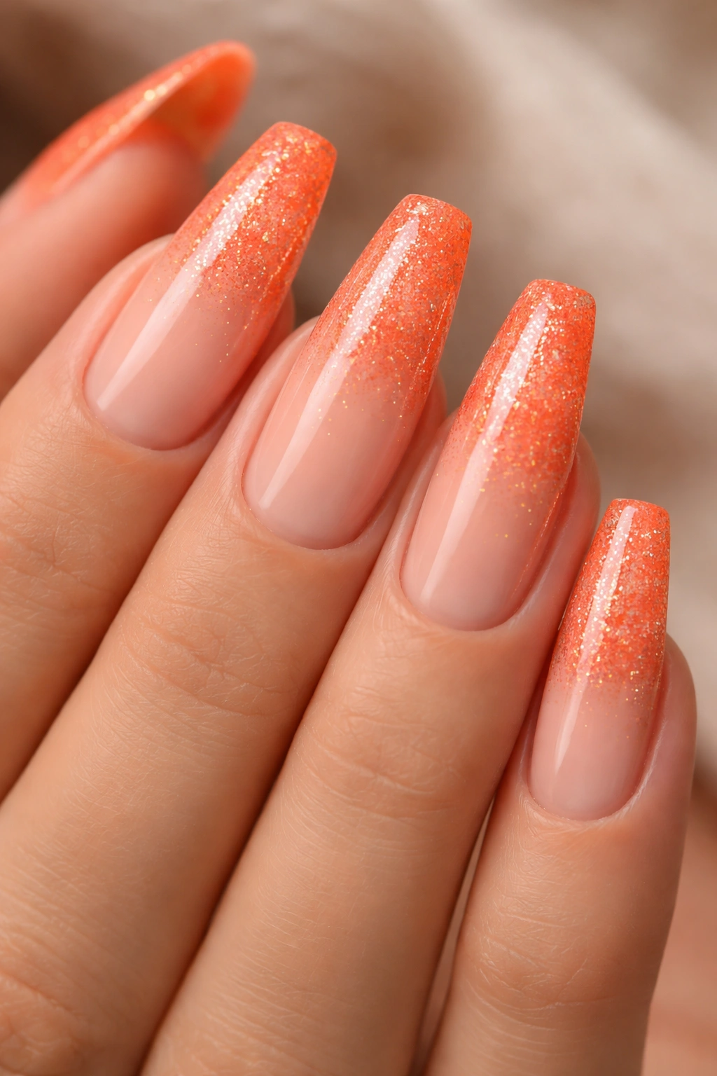 Close-up of coral-orange glitter fade on a sheer nude base.