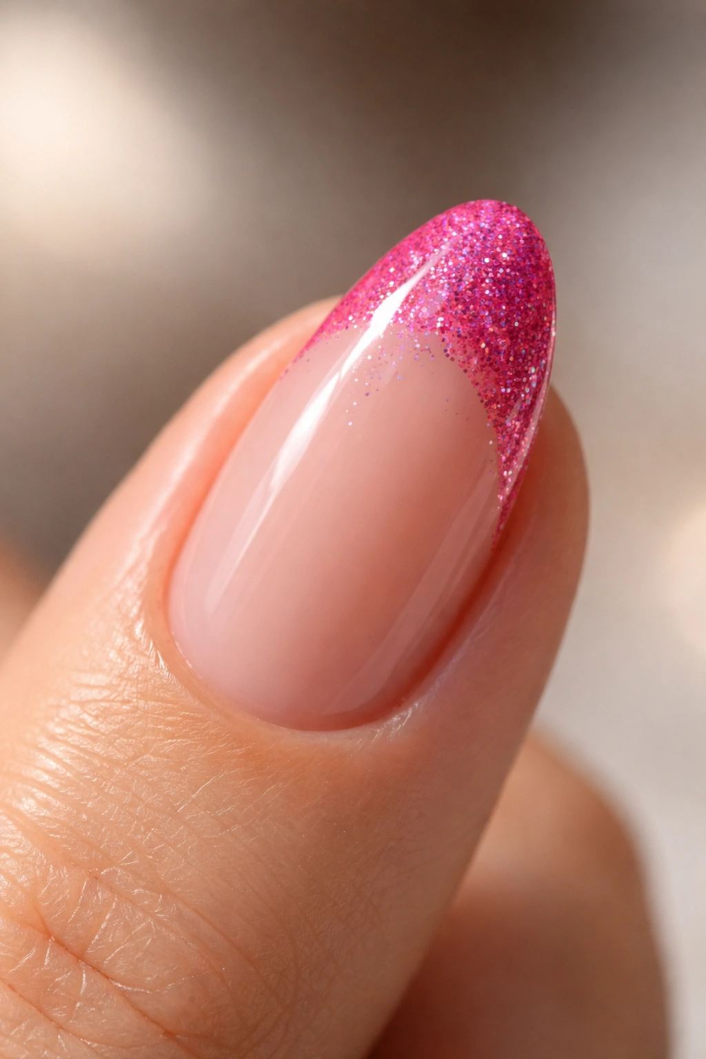 Close-up of a short almond nail with glittery hot pink French tip