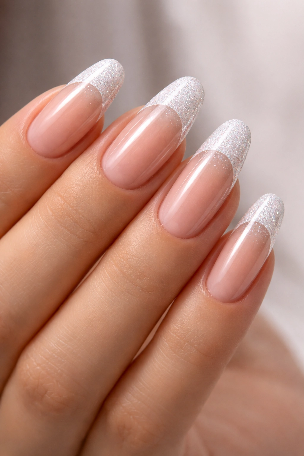 Close-up of long round acrylic nails with clear base and glitter tips under studio lighting
