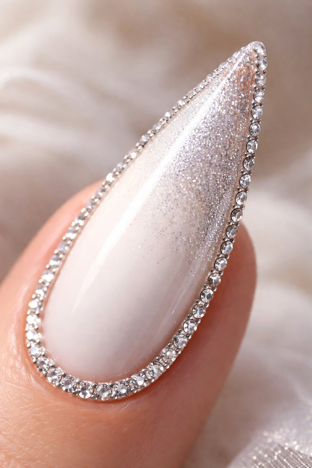 Close-up of a stiletto nail with glitter gradient and rhinestone border