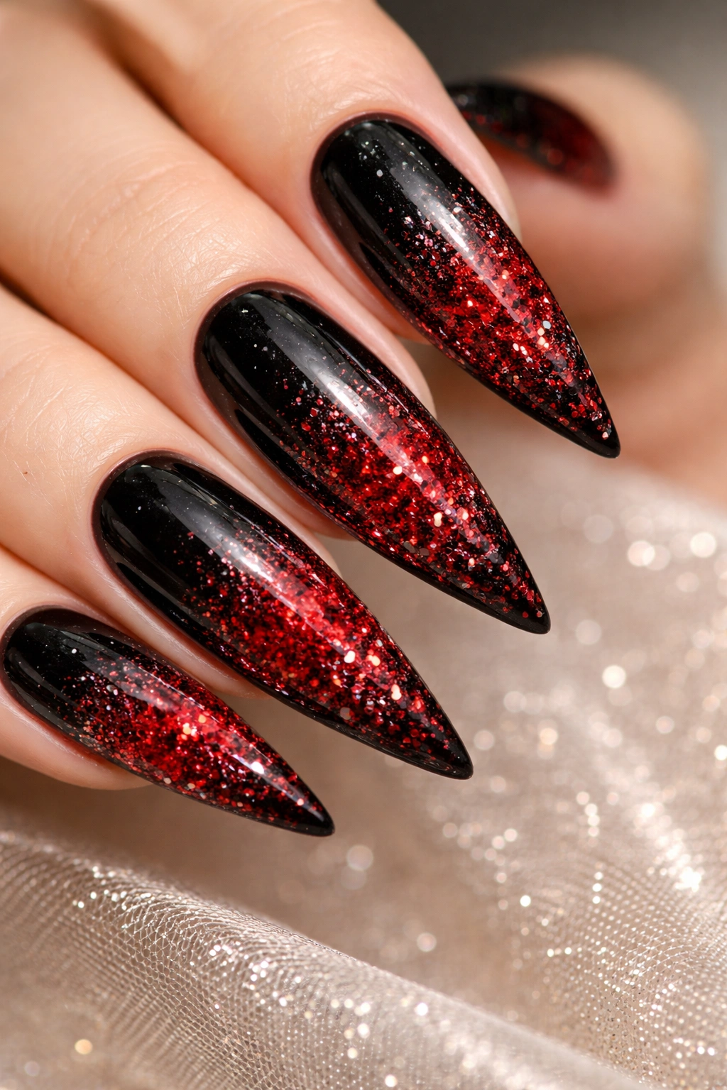 Close-up of black-to-red glitter ombre stiletto nails with sparkling texture