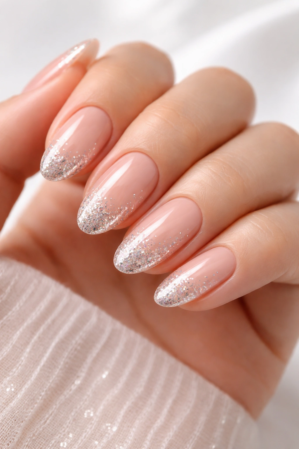 Close-up of nails with nude base and glitter tips on the ends