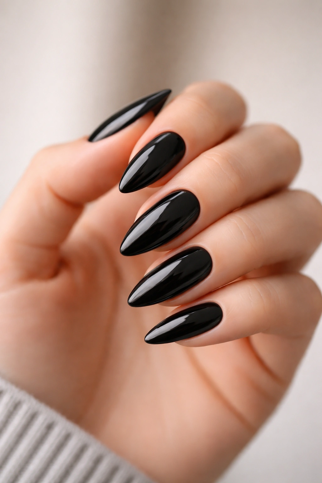 Close-up of glossy black almond nails with high shine on a pale hand