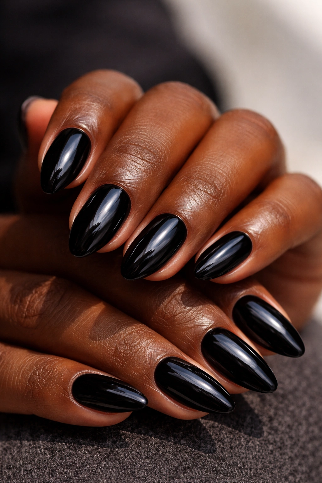 Close-up of short almond nails in glossy jet-black with high shine on dark skin