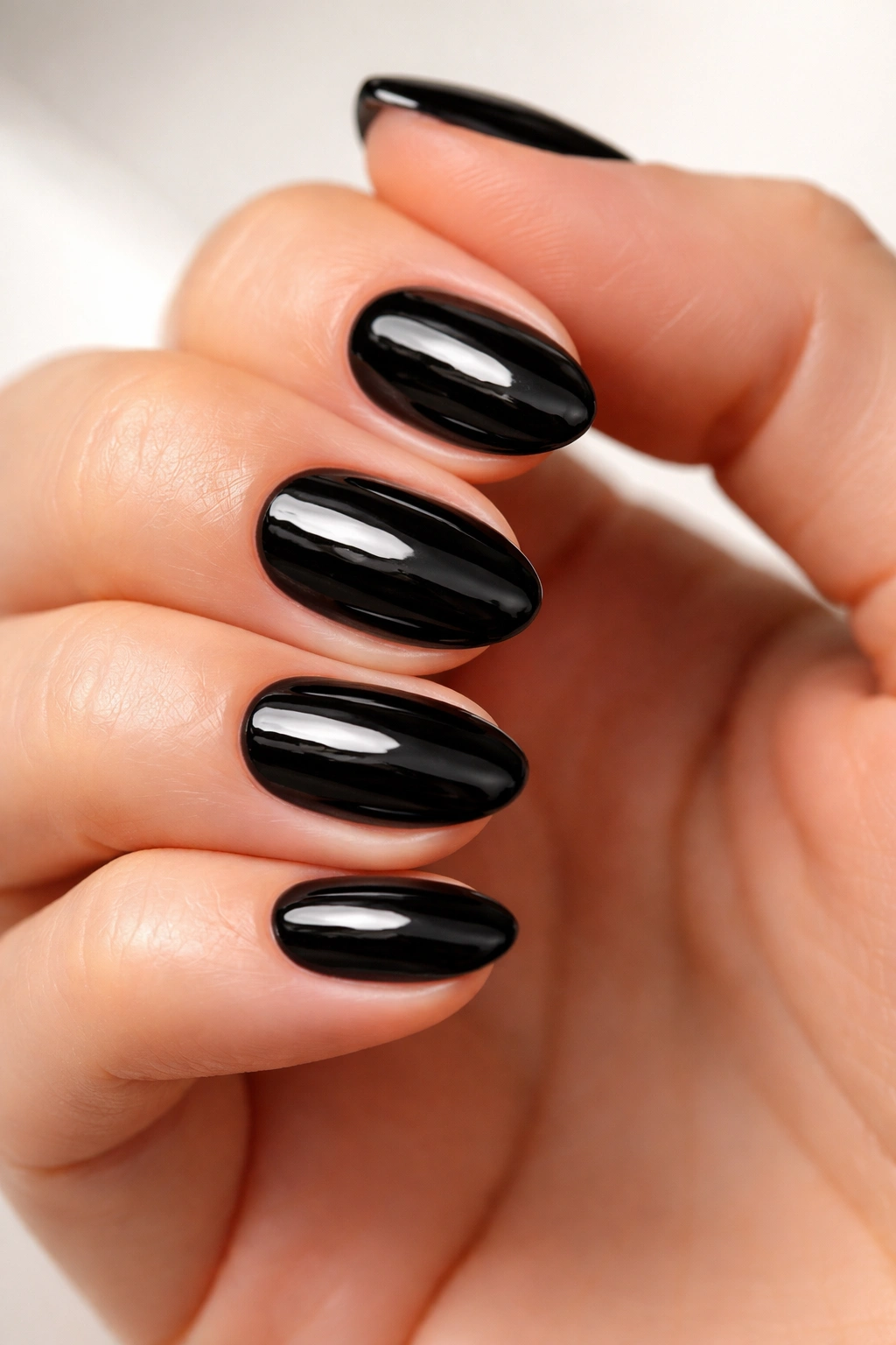 Close-up of ultra-short glossy black almond nails on a neutral background