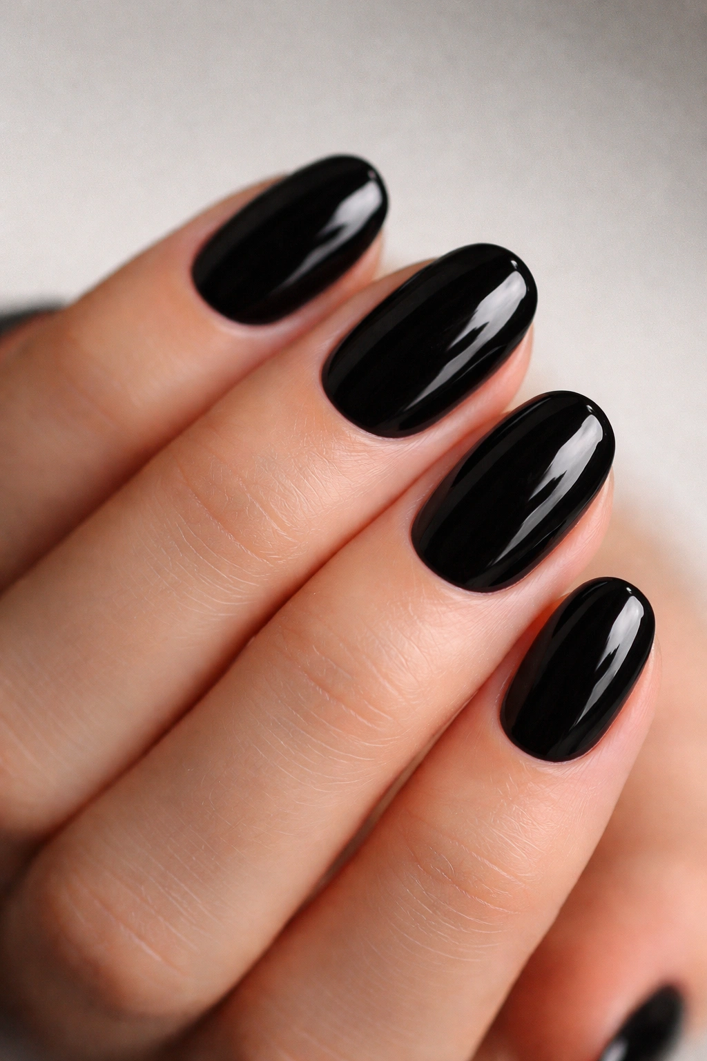 Close-up of short oval nails painted glossy black with high shine