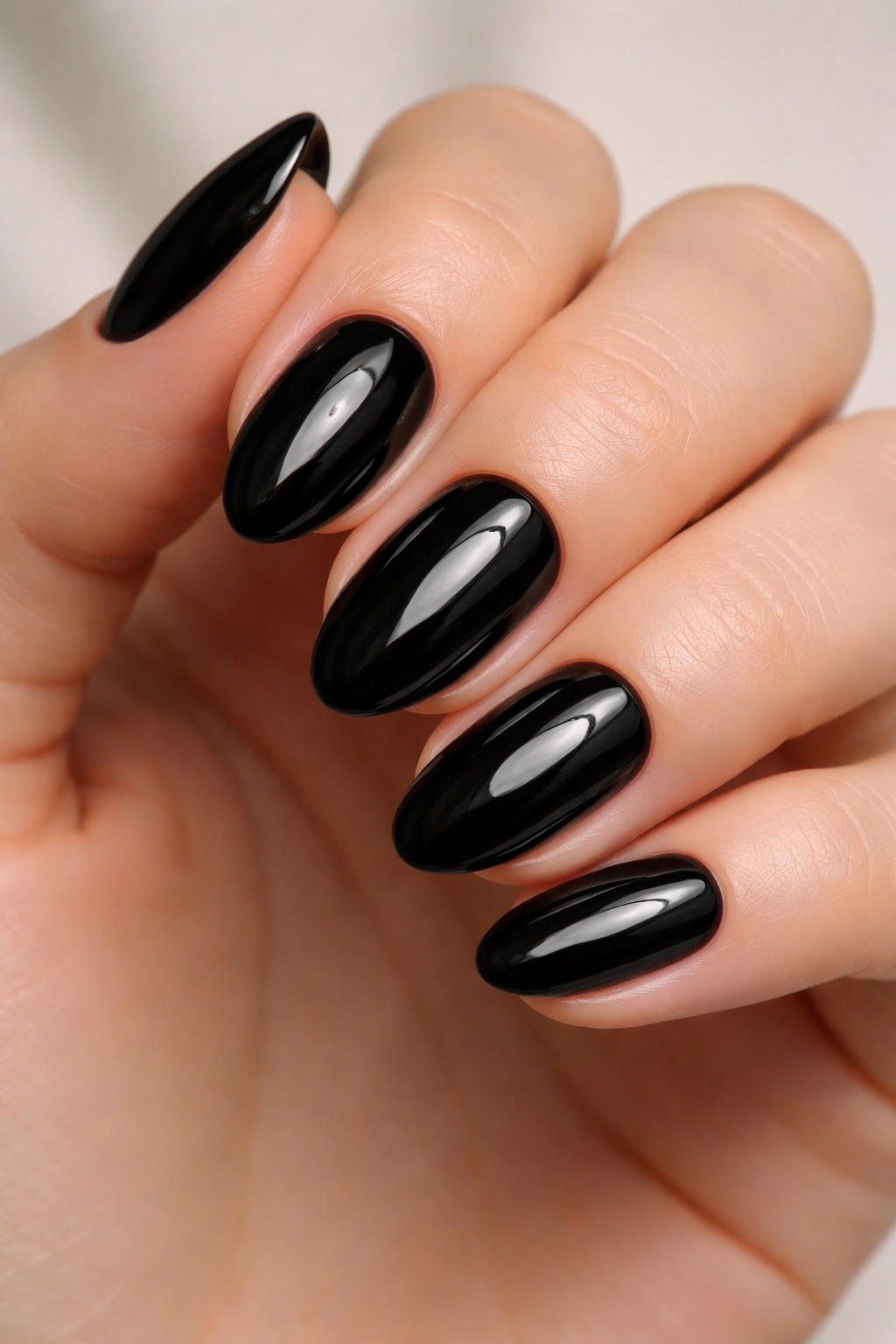 Close-up of glossy black short almond nails with clean cuticles on a neutral surface