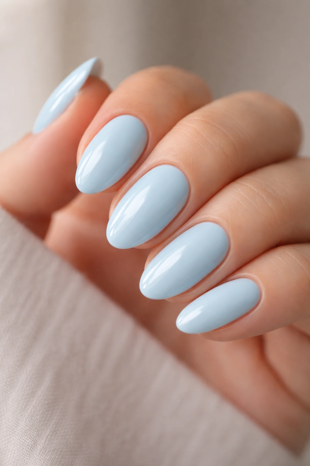 Close-up of short almond nails painted glossy baby blue with high shine on a neutral background