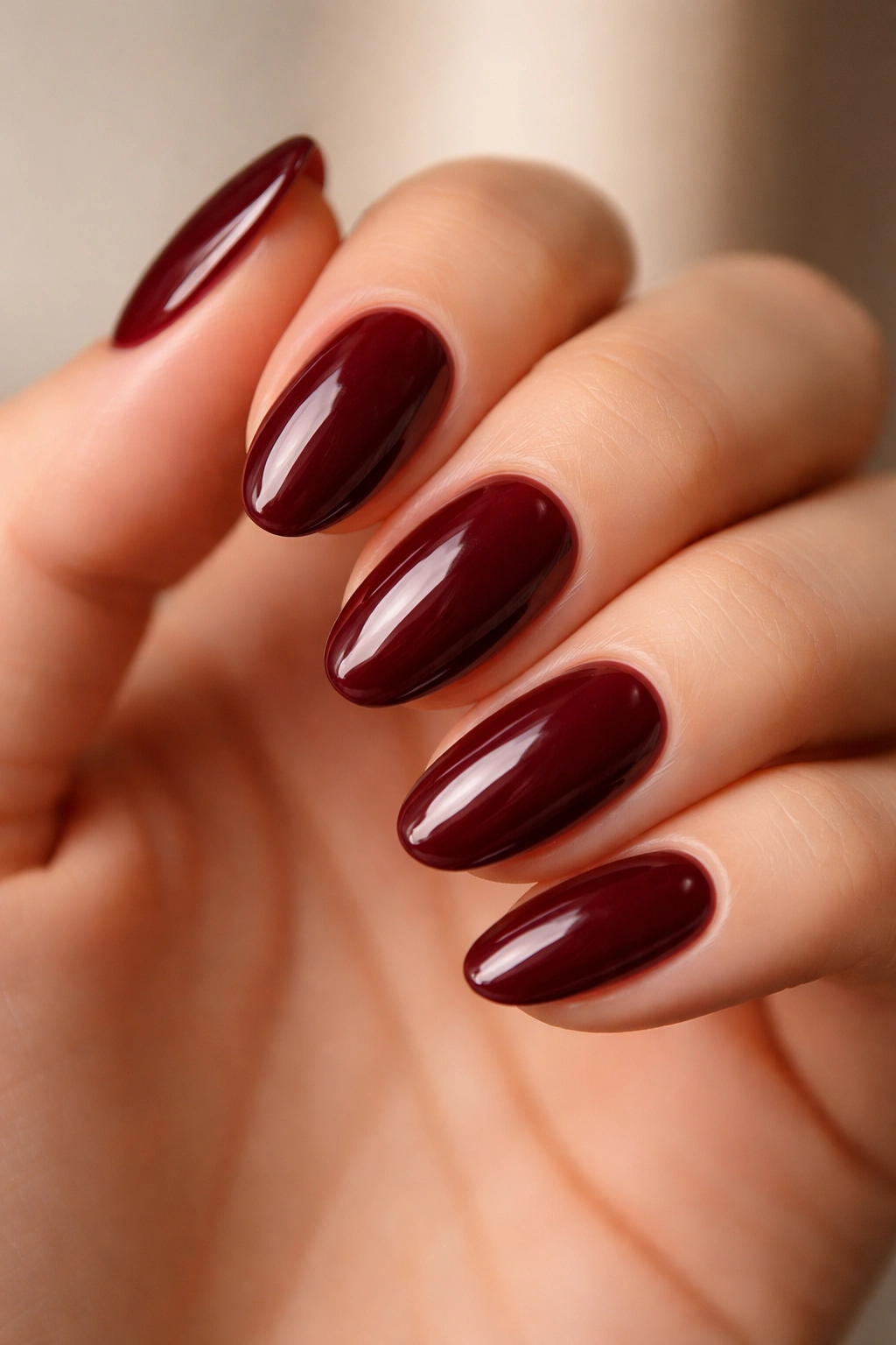 Close-up of short burgundy almond nails with a glossy mirror finish