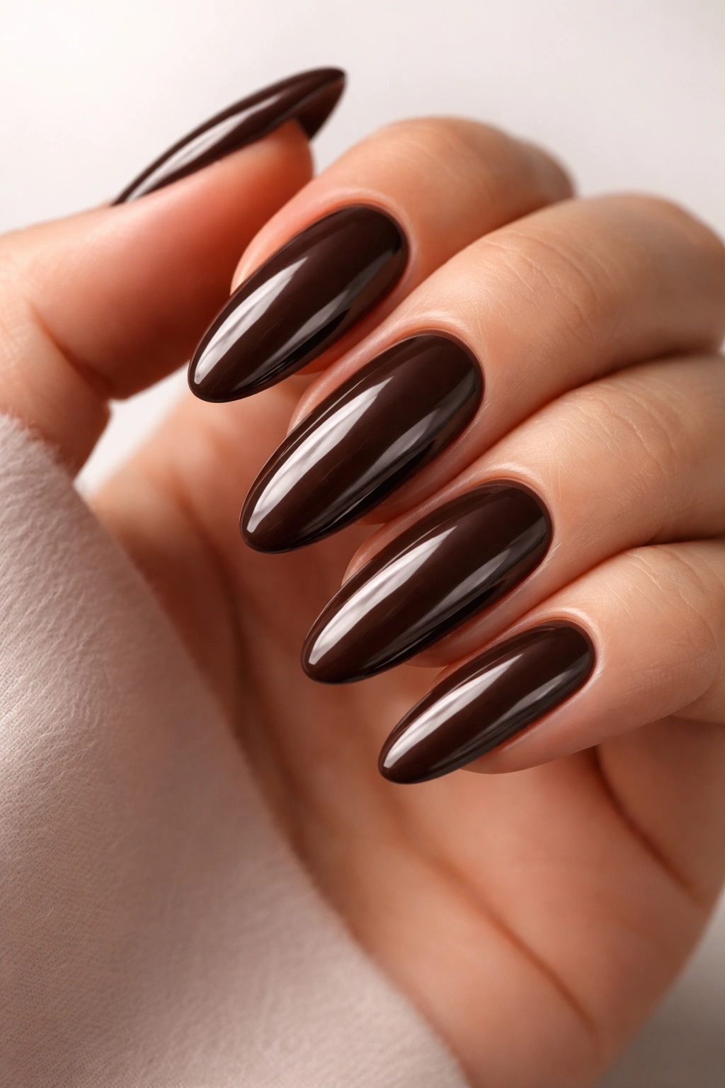 Close-up of long round nails with glossy chocolate brown finish reflecting studio light