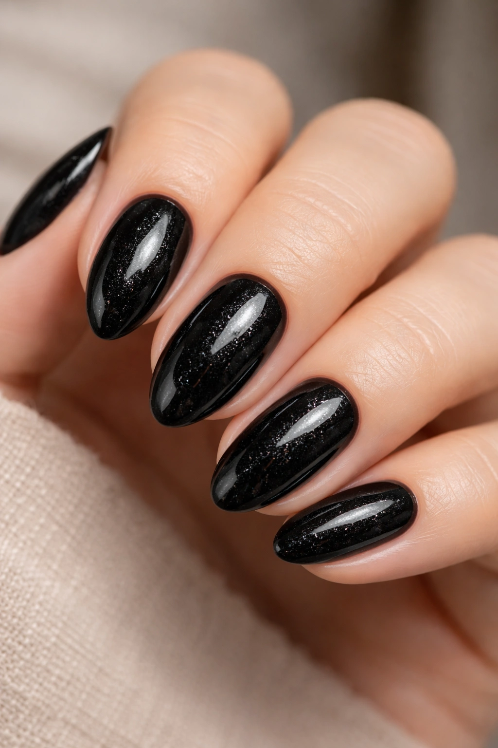 Close-up of glossy black almond nails with micro glitter