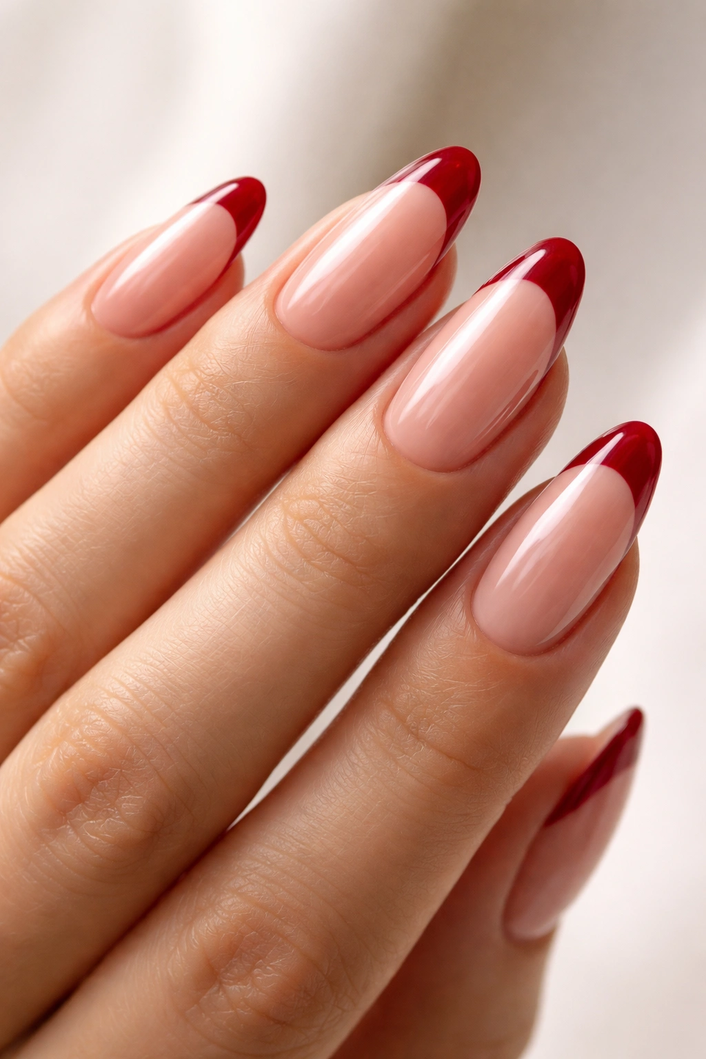 Close-up of almond nails with sheer nude base and glossy cherry-red tips.
