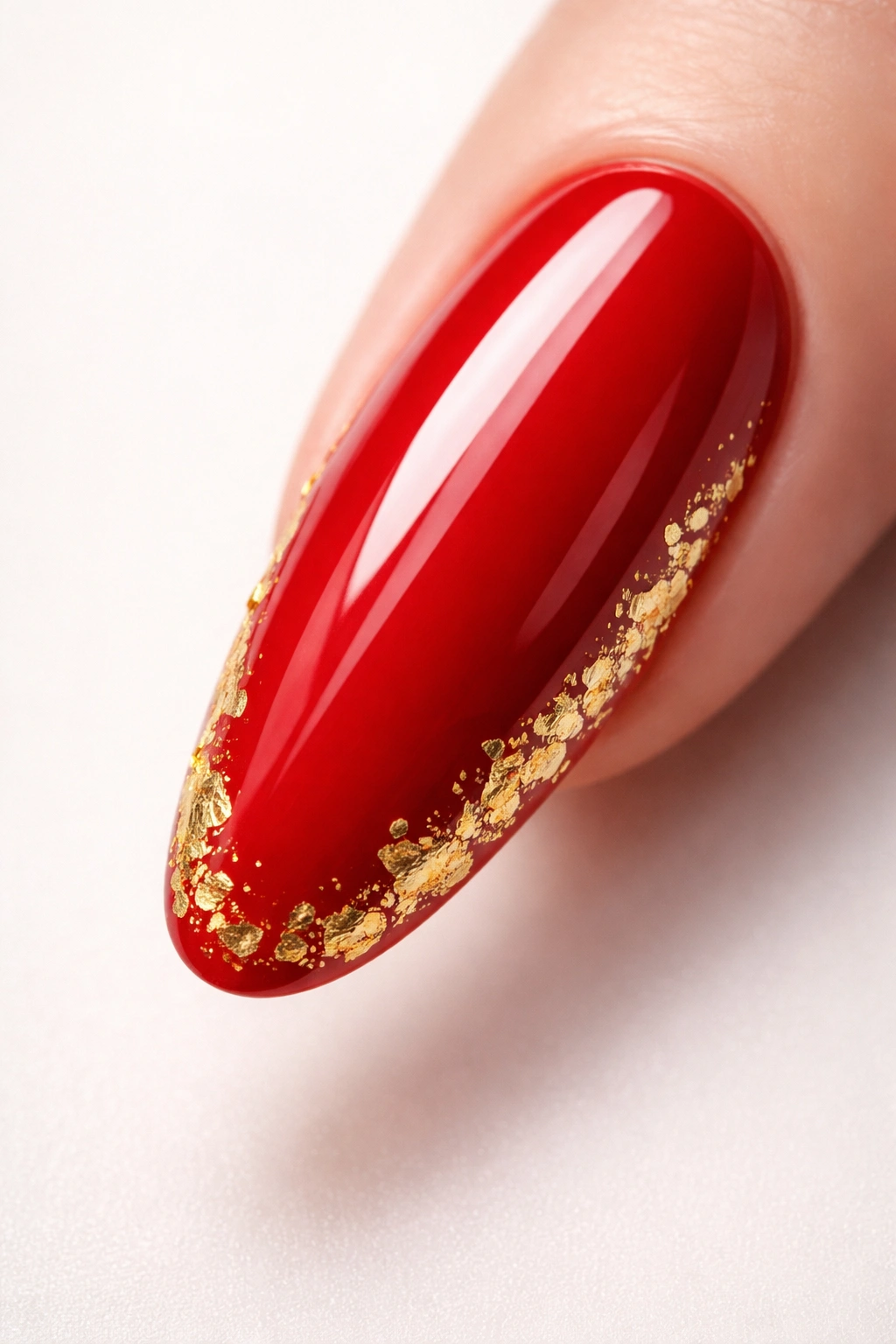 Close-up of a glossy red oval nail with gold leaf accents
