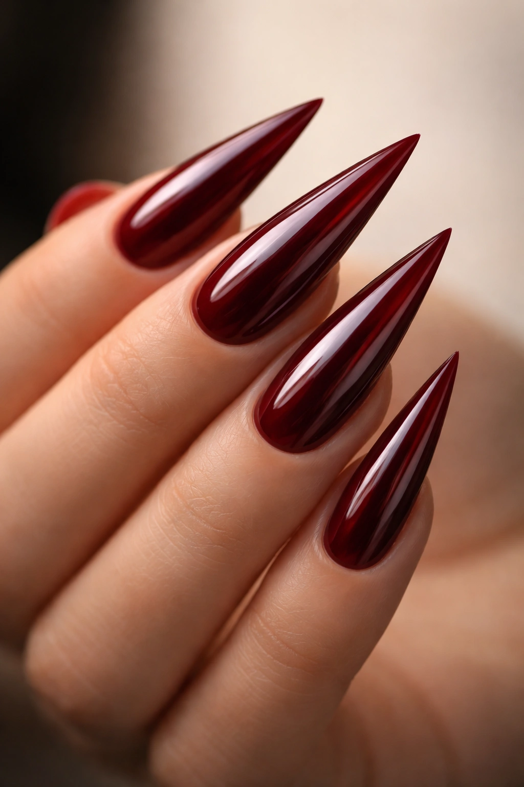 Close-up of glossy dark red stiletto nails with sharp points.