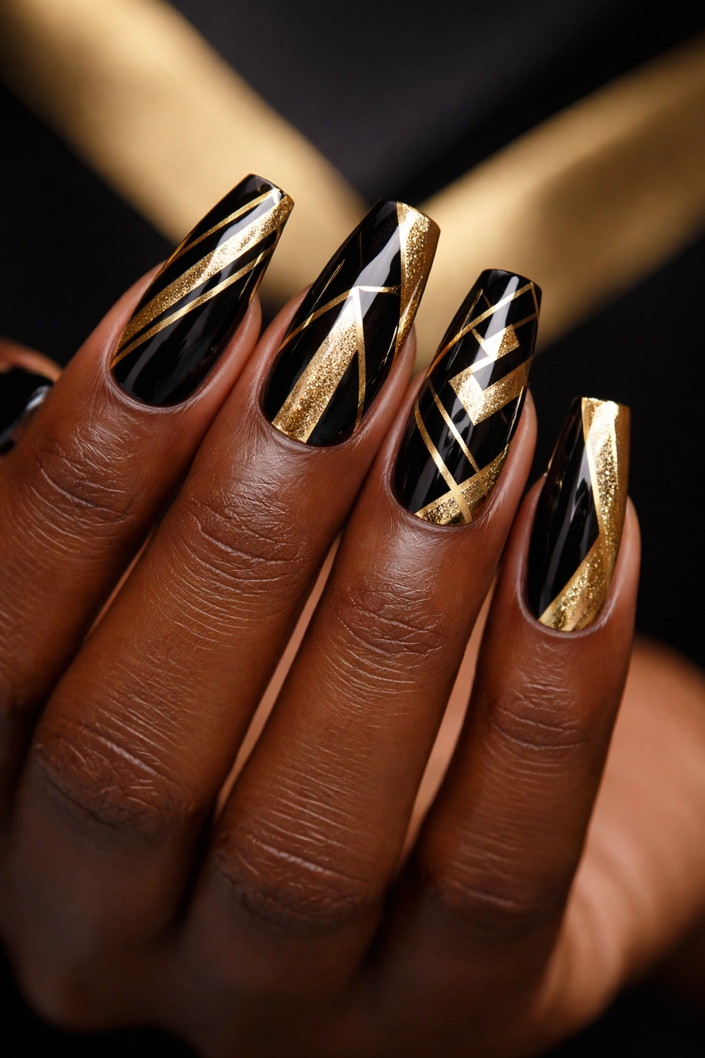 Dark-skinned hand with gold and black geometric nail design