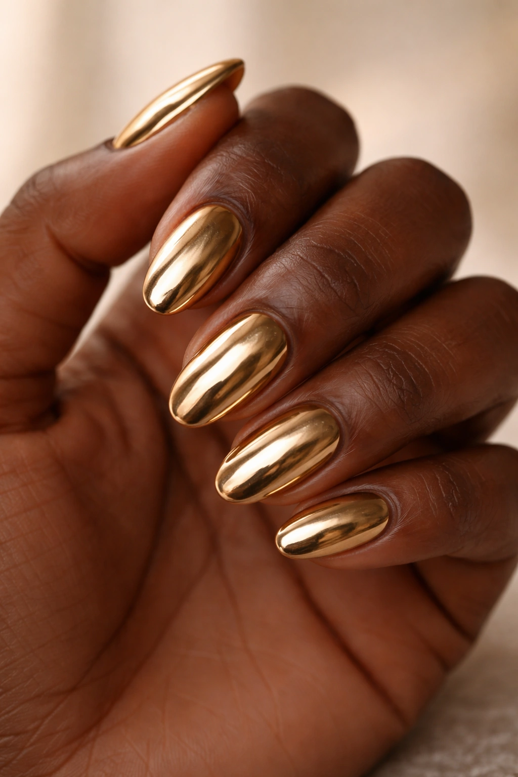 Close-up of a hand with short almond nails in warm gold chrome finish