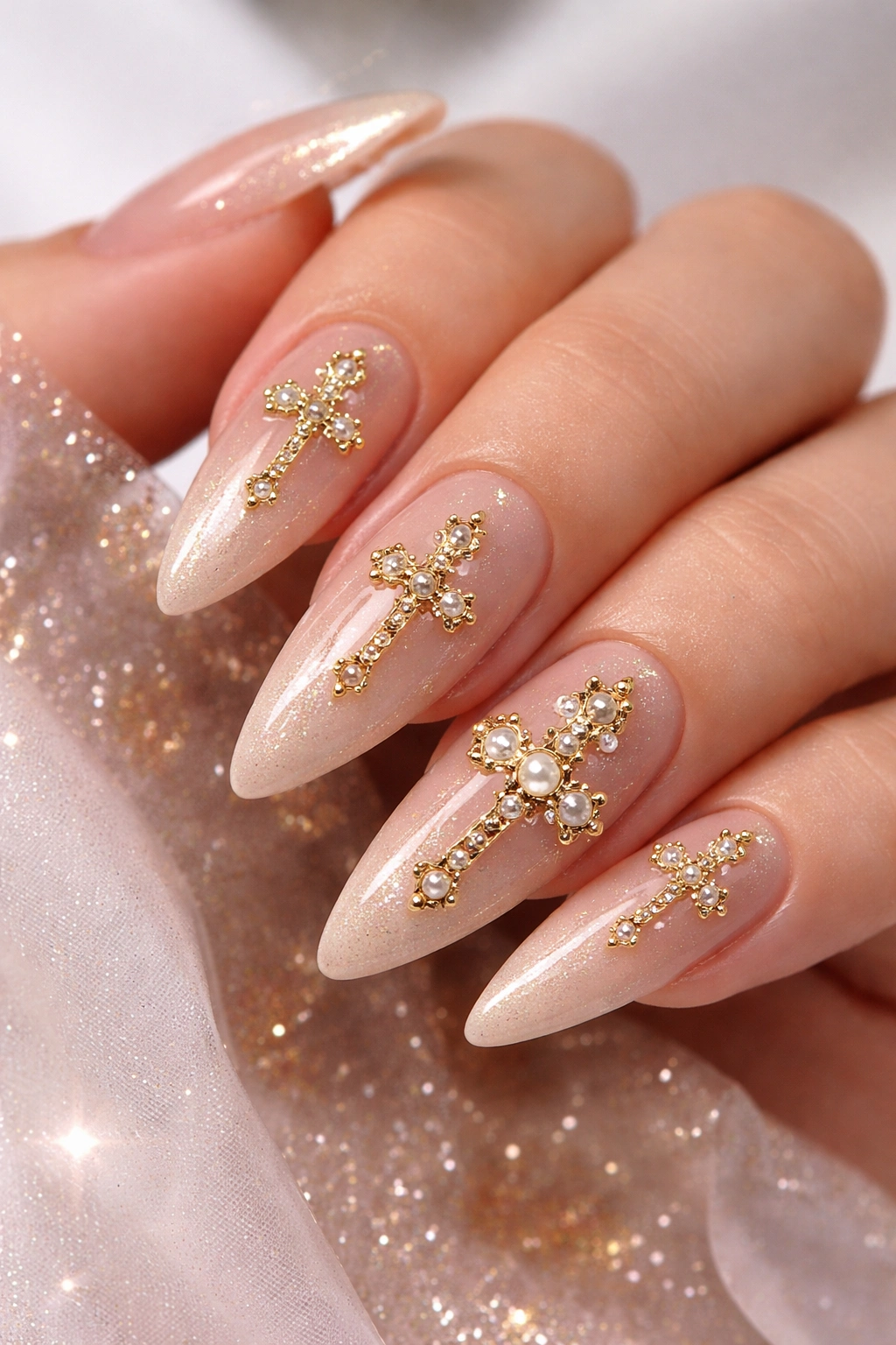 Almond acrylic nails with gold cross charms on nude base