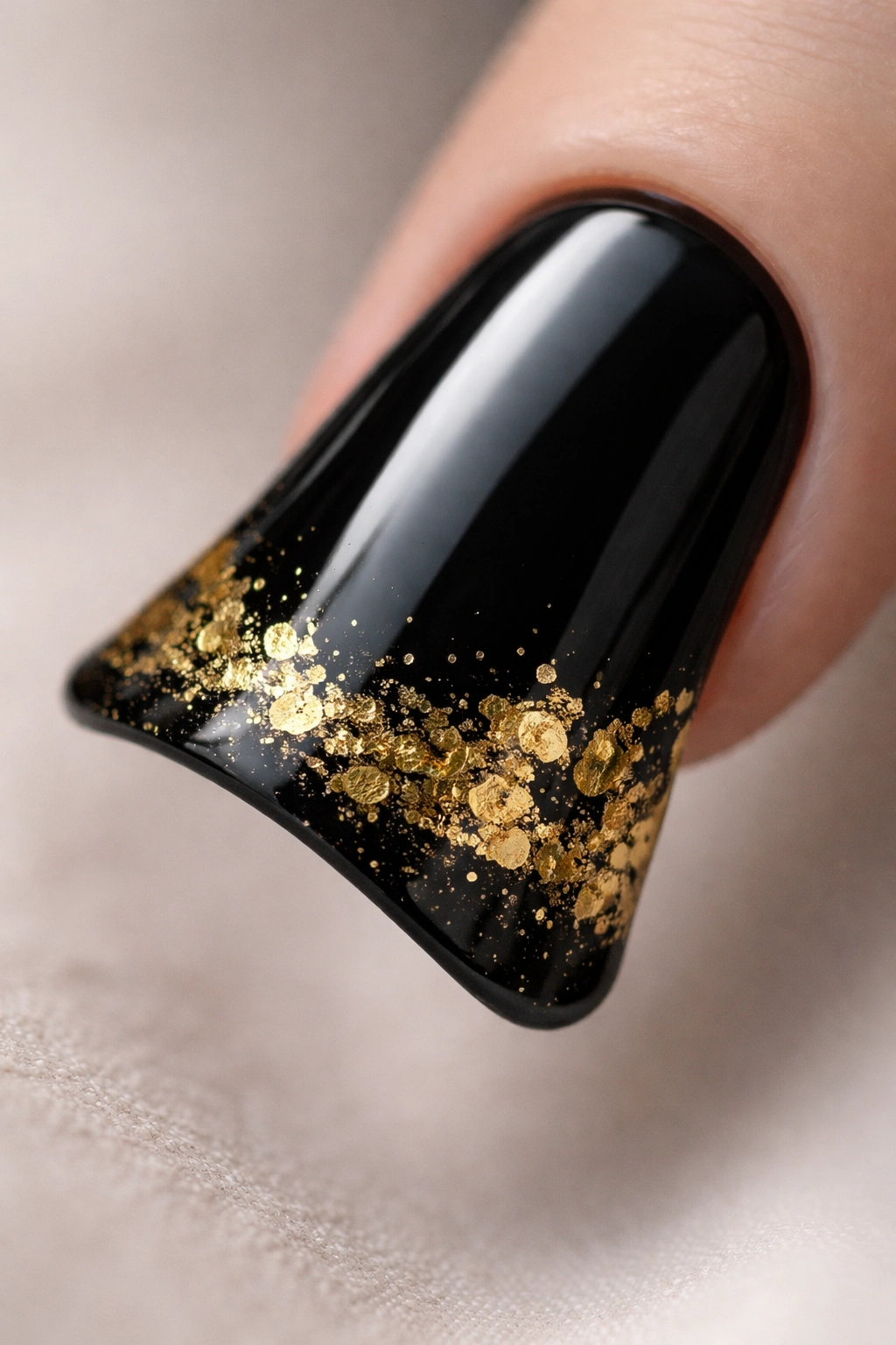 Close-up of a duck nail with a black base and irregular gold foil on the curved tip