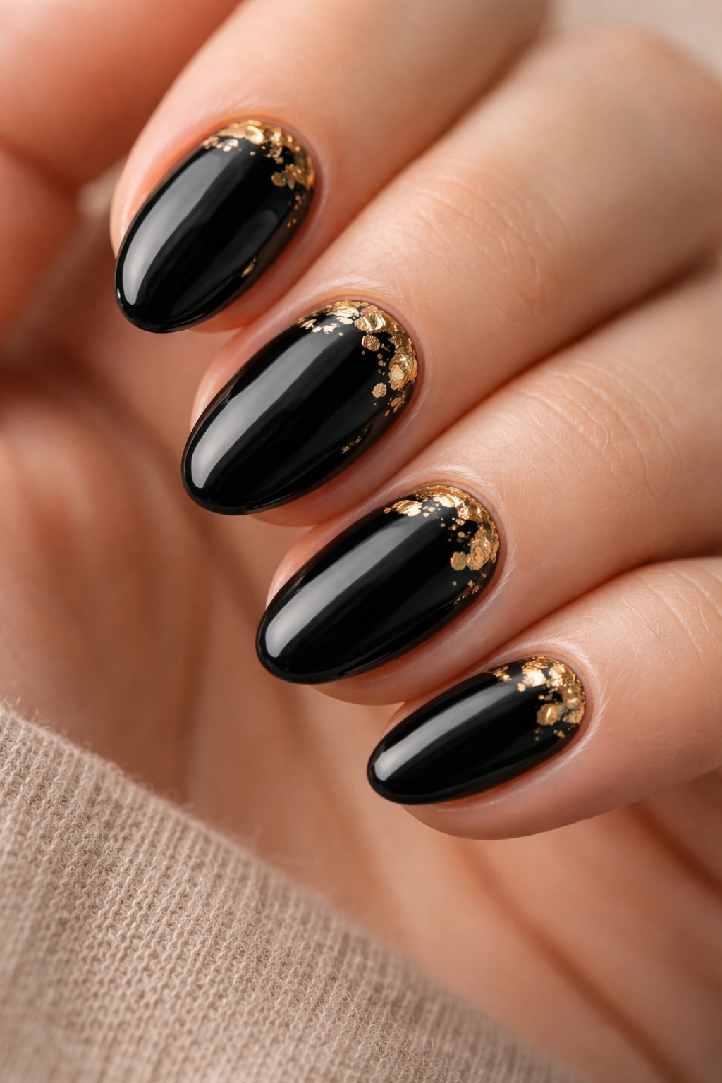 Close-up of short black almond nails with gold foil accents