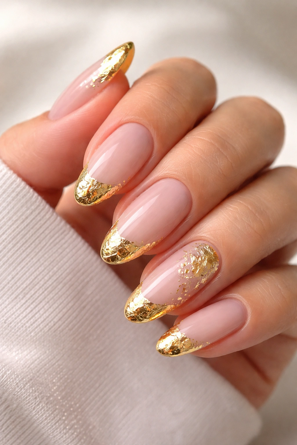Close-up of nails with sheer nude base and irregular gold foil on the tips