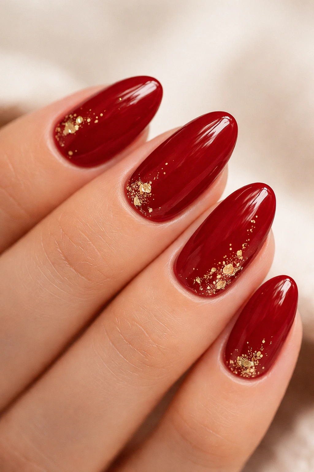 Cherry red nails with gold foil accents on a short almond shape