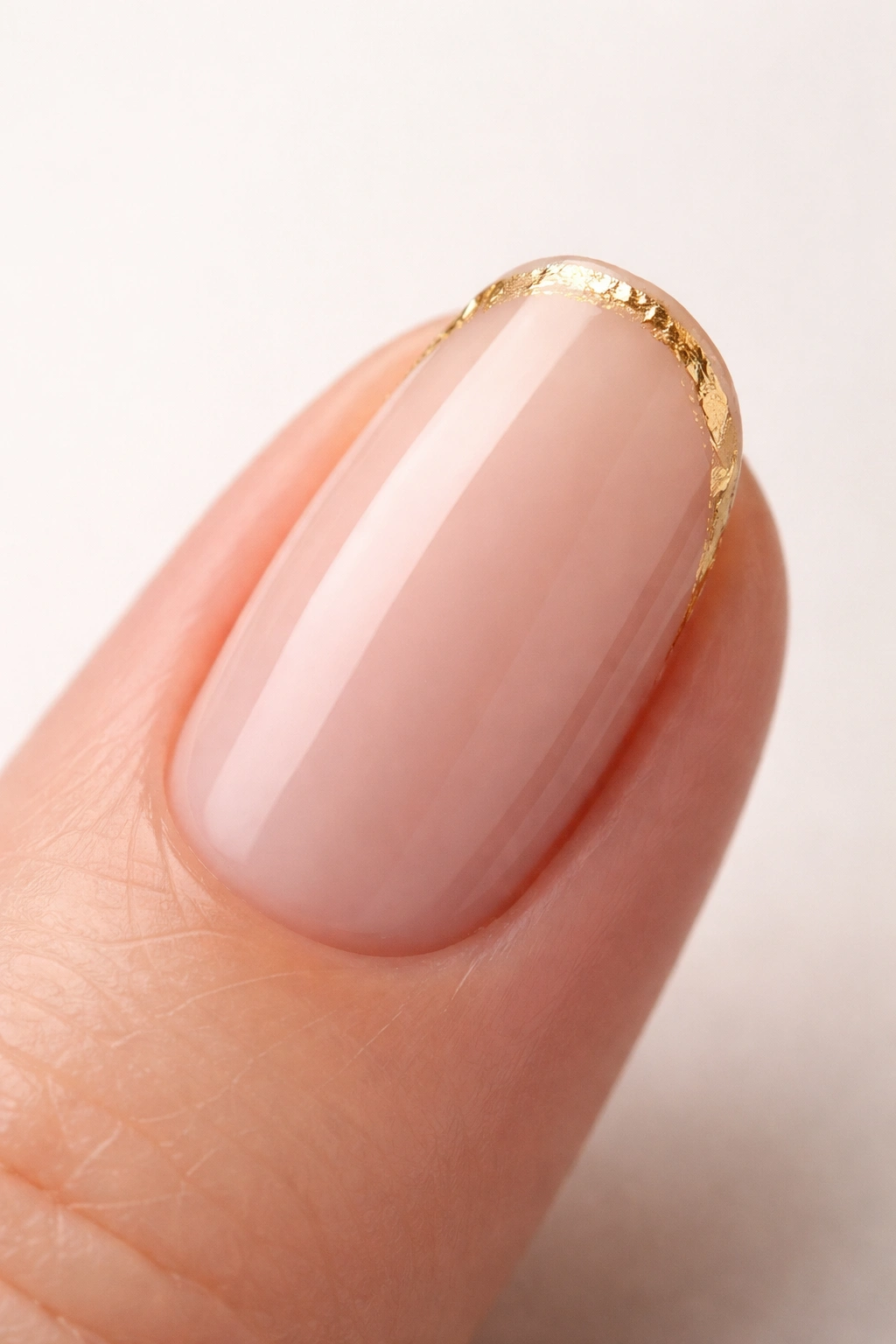 Close-up of a single nude nail with a thin gold foil accent near the cuticle.