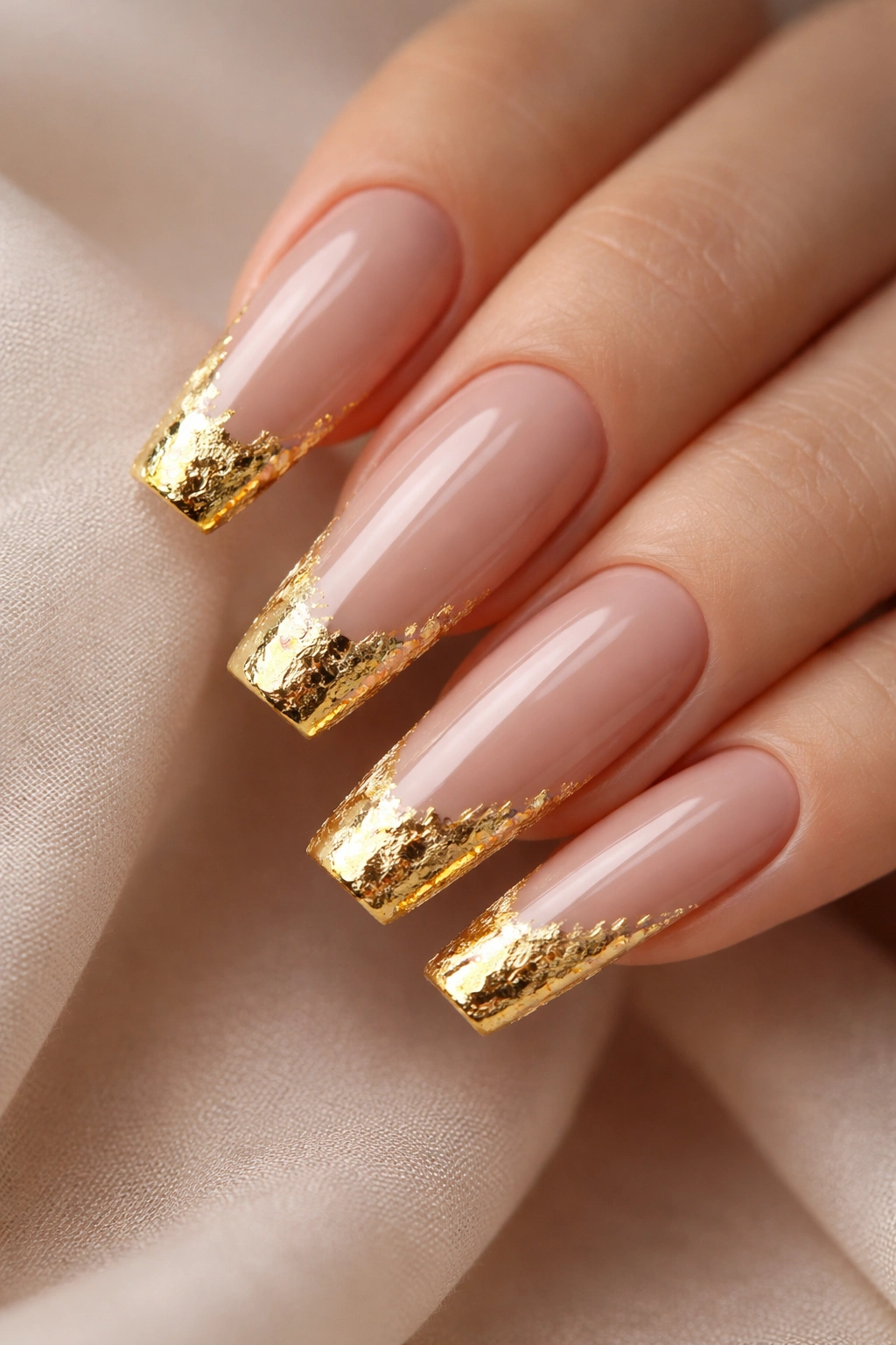 Close-up of long coffin nails with nude base and gold foil tips