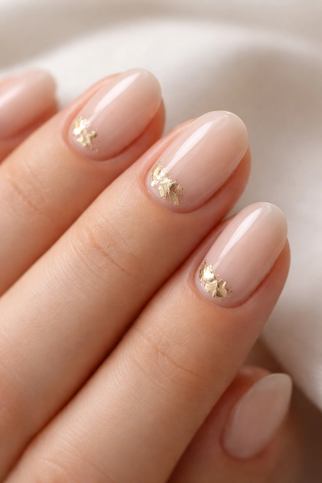 Nude base short oval nails with small gold foil patches near cuticle
