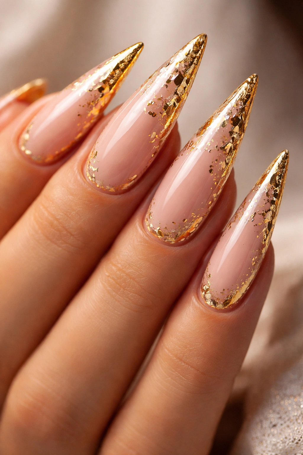 Close-up of stiletto nails with gold foil accents along the edges on a neutral background