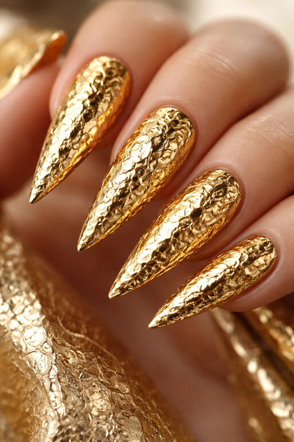 Close-up of gold foil textured stiletto nails on neutral background