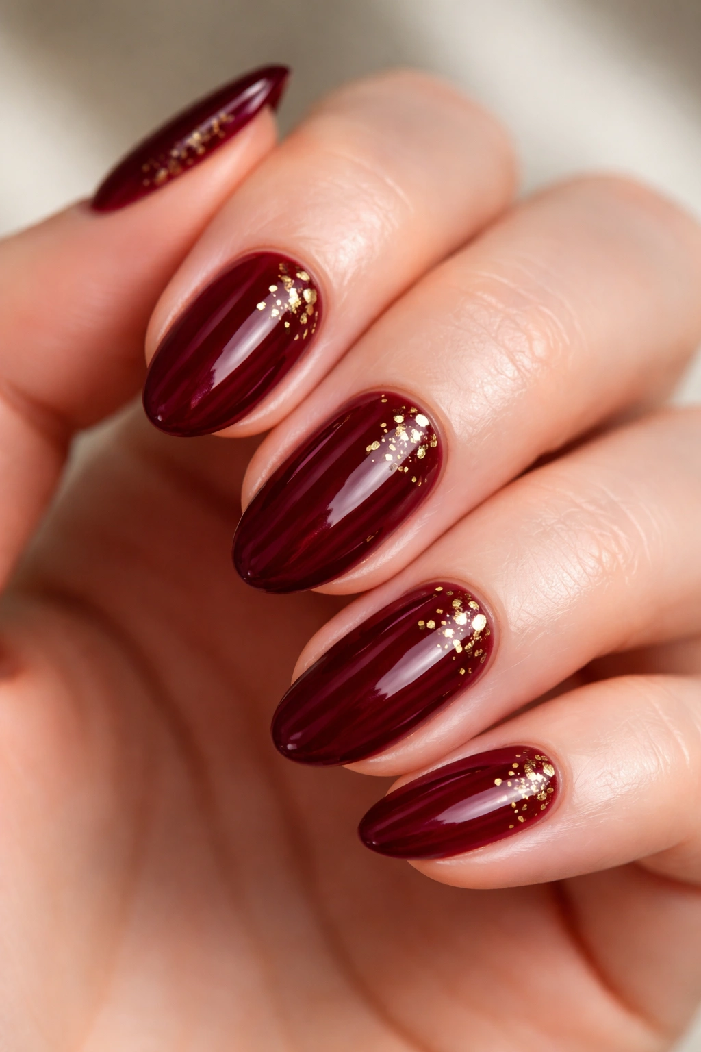 Close-up of short almond nails with subtle gold foil flecks on wine red polish