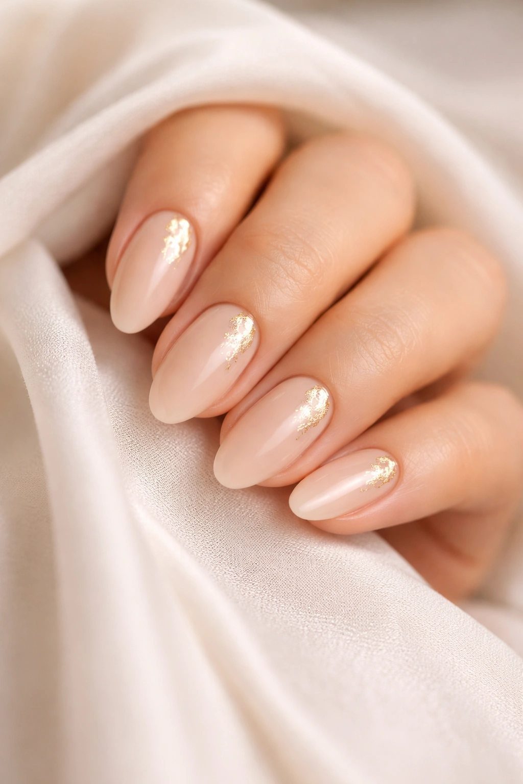 Nude almond nails with subtle gold foil accents on a pale base
