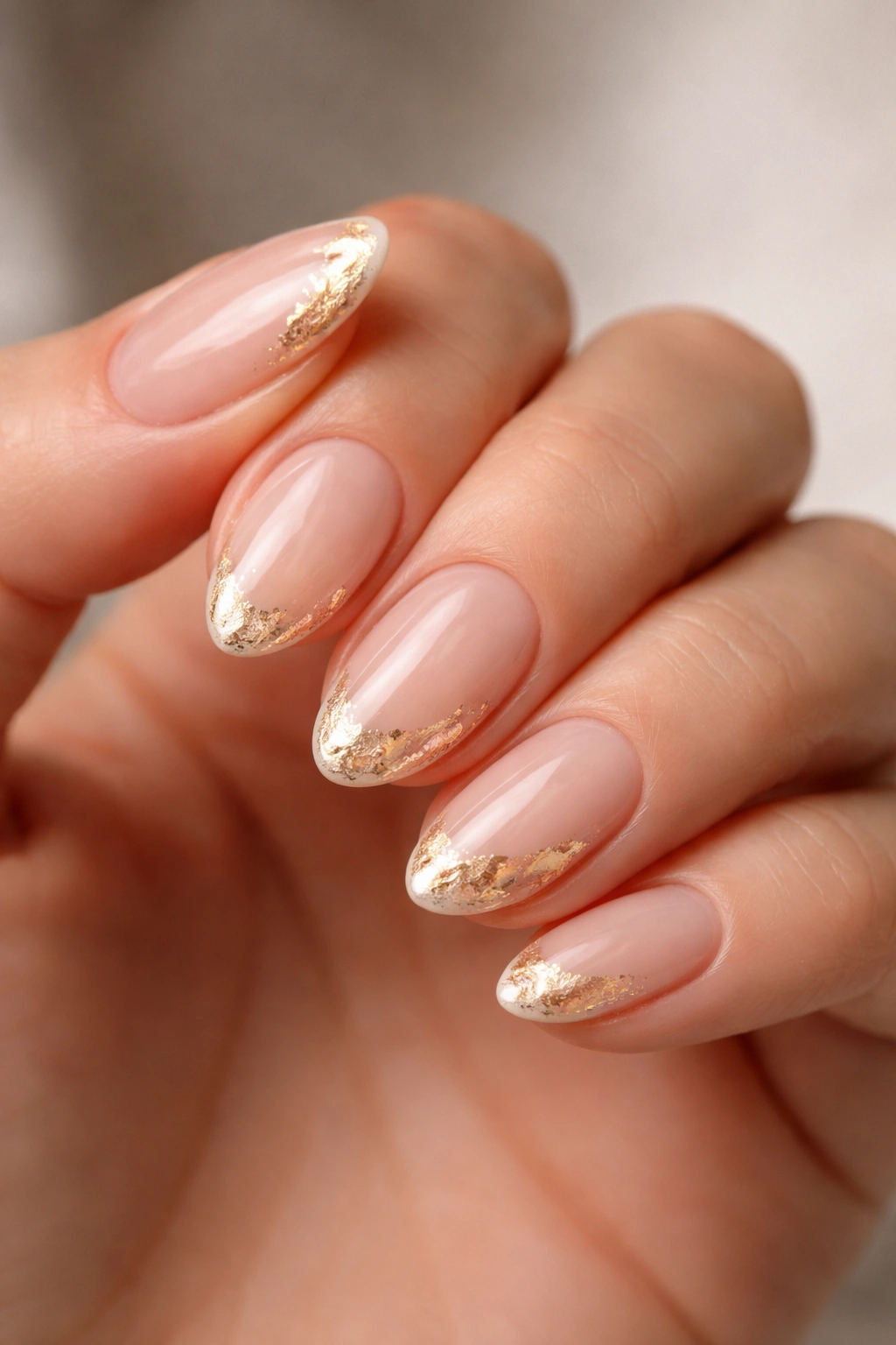 Close-up of short almond nails with gold foil accents on a neutral base