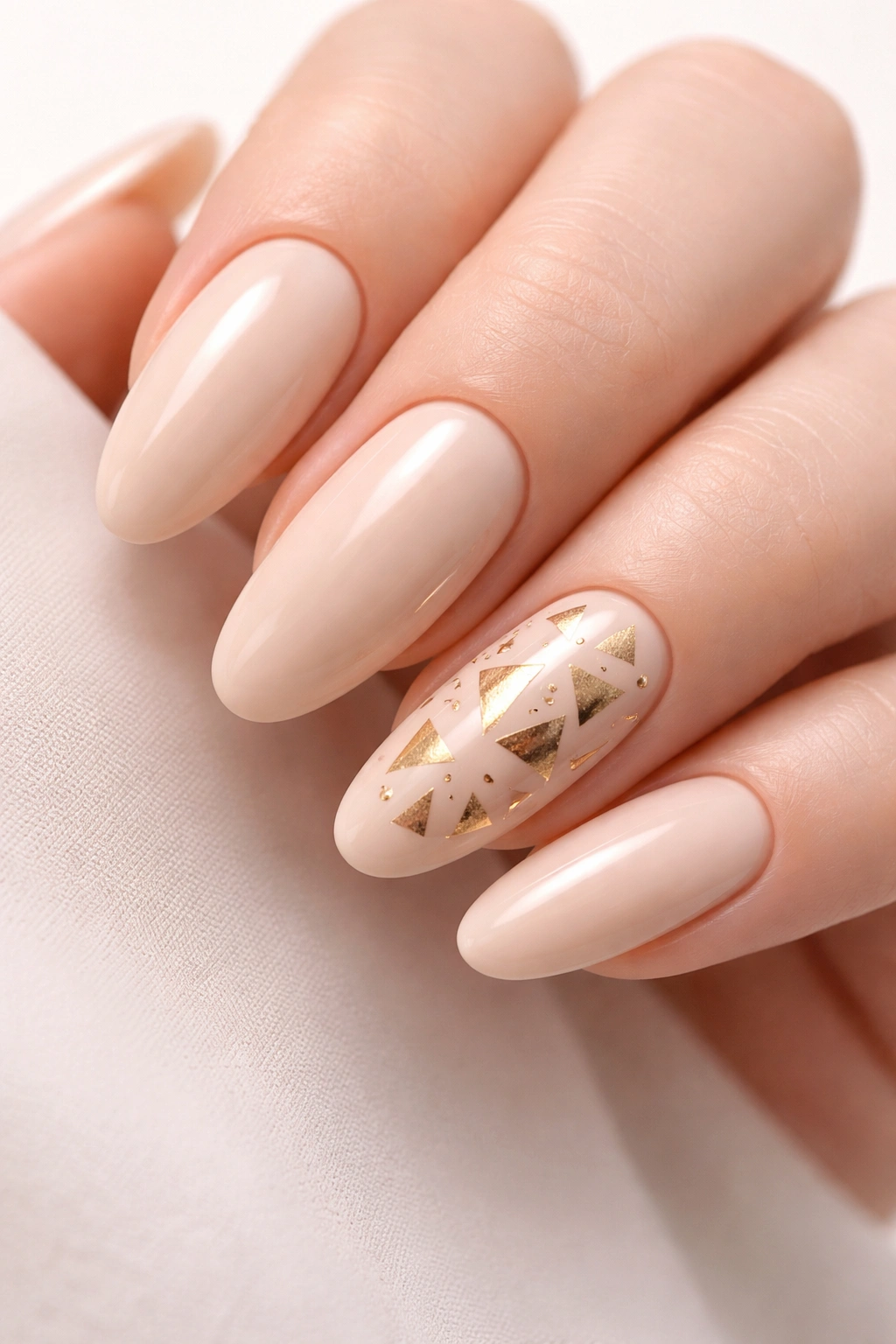 Close-up of nude nails with a gold triangle accent nail in abstract arrangement