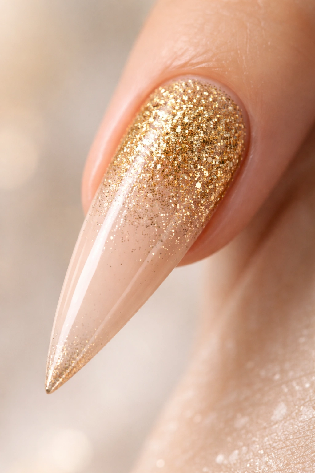 Gold glitter gradient on a stiletto nail with dense glitter at base fading to nude tip