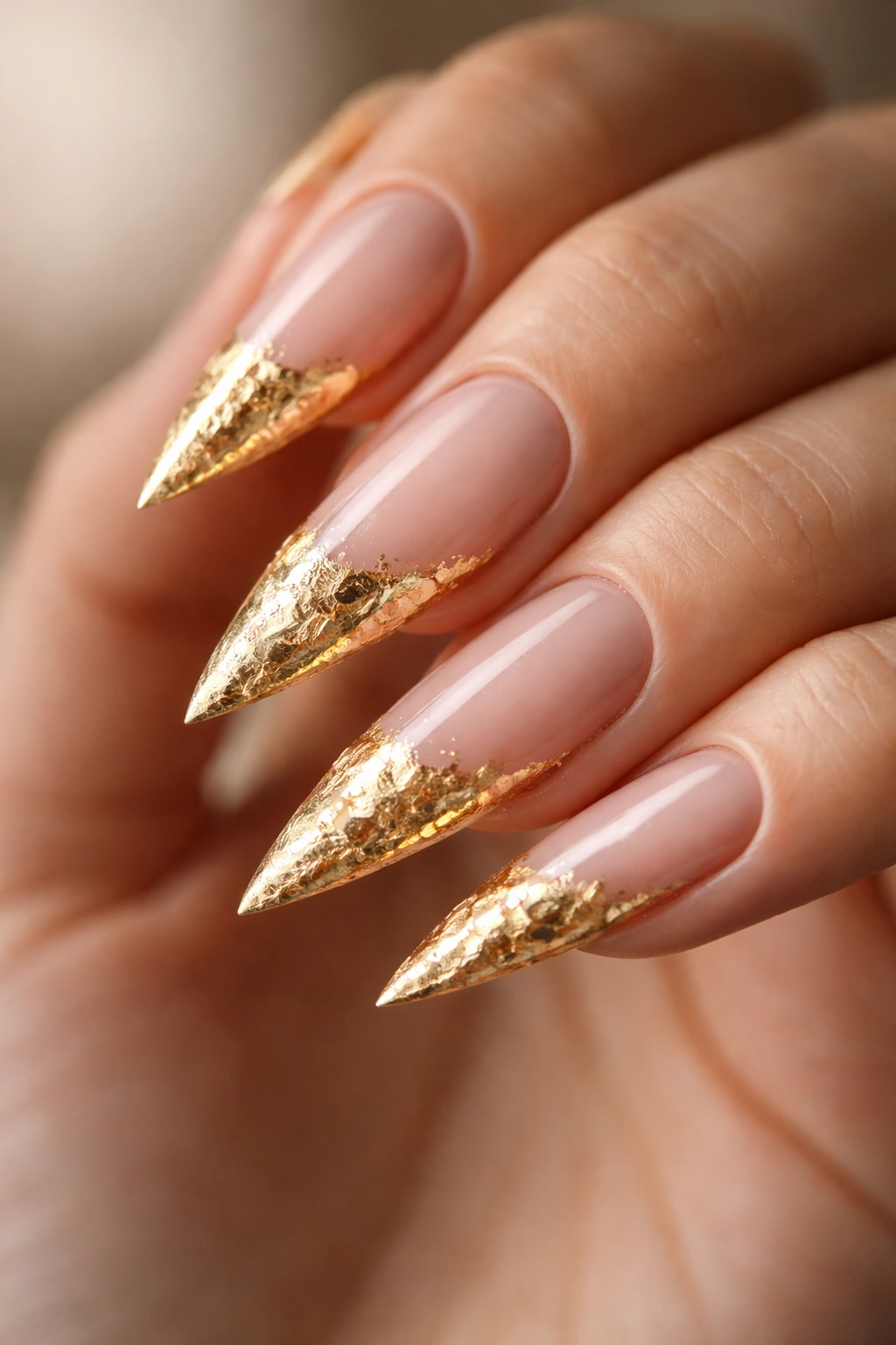Close-up of stiletto nails with irregular gold leaf on tips.