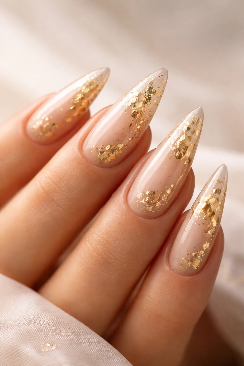 Close-up of gold leaf glamour nails with neutral base and gold flecks