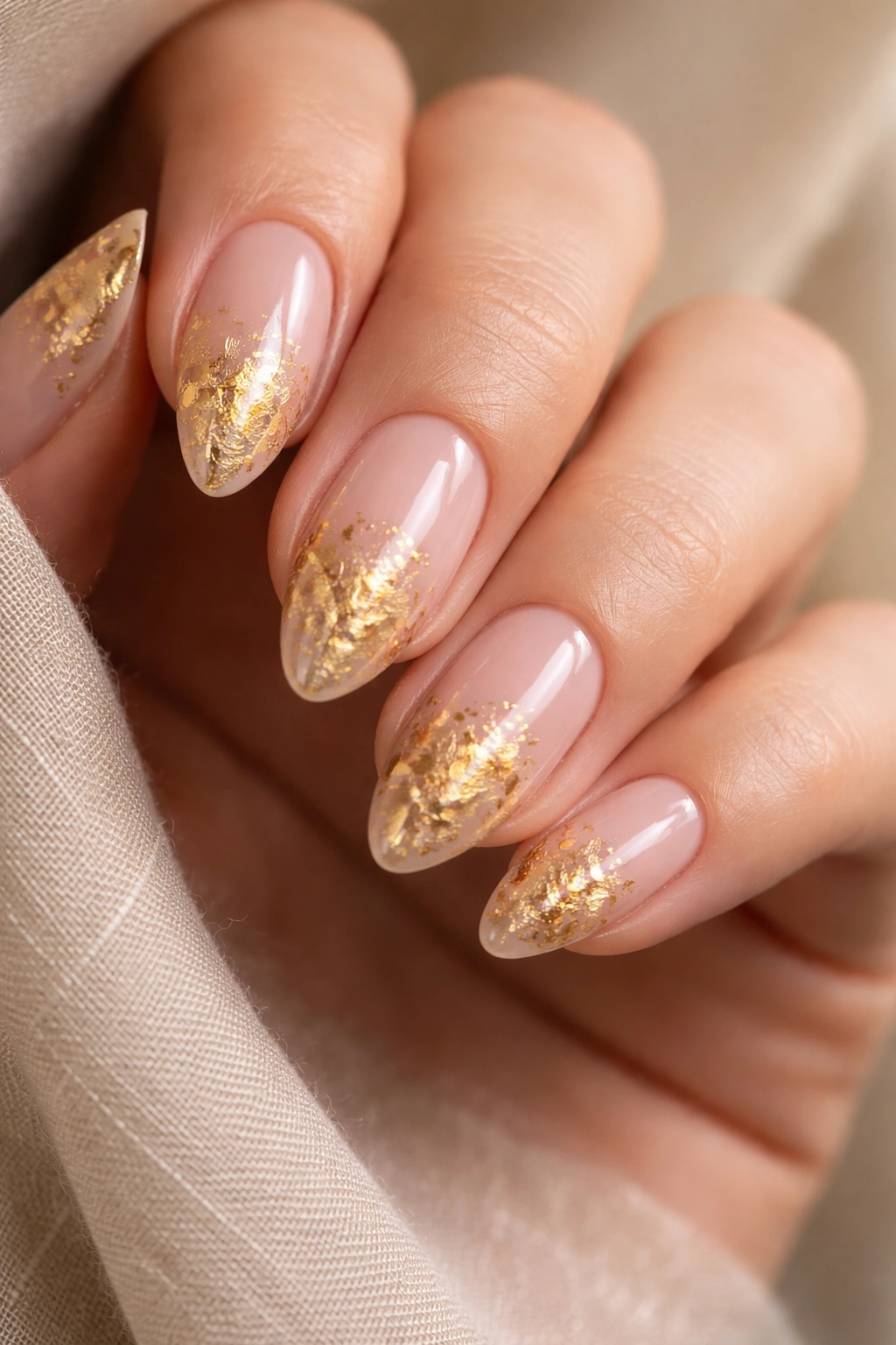 Almond nails with irregular gold leaf on a blush nude base.
