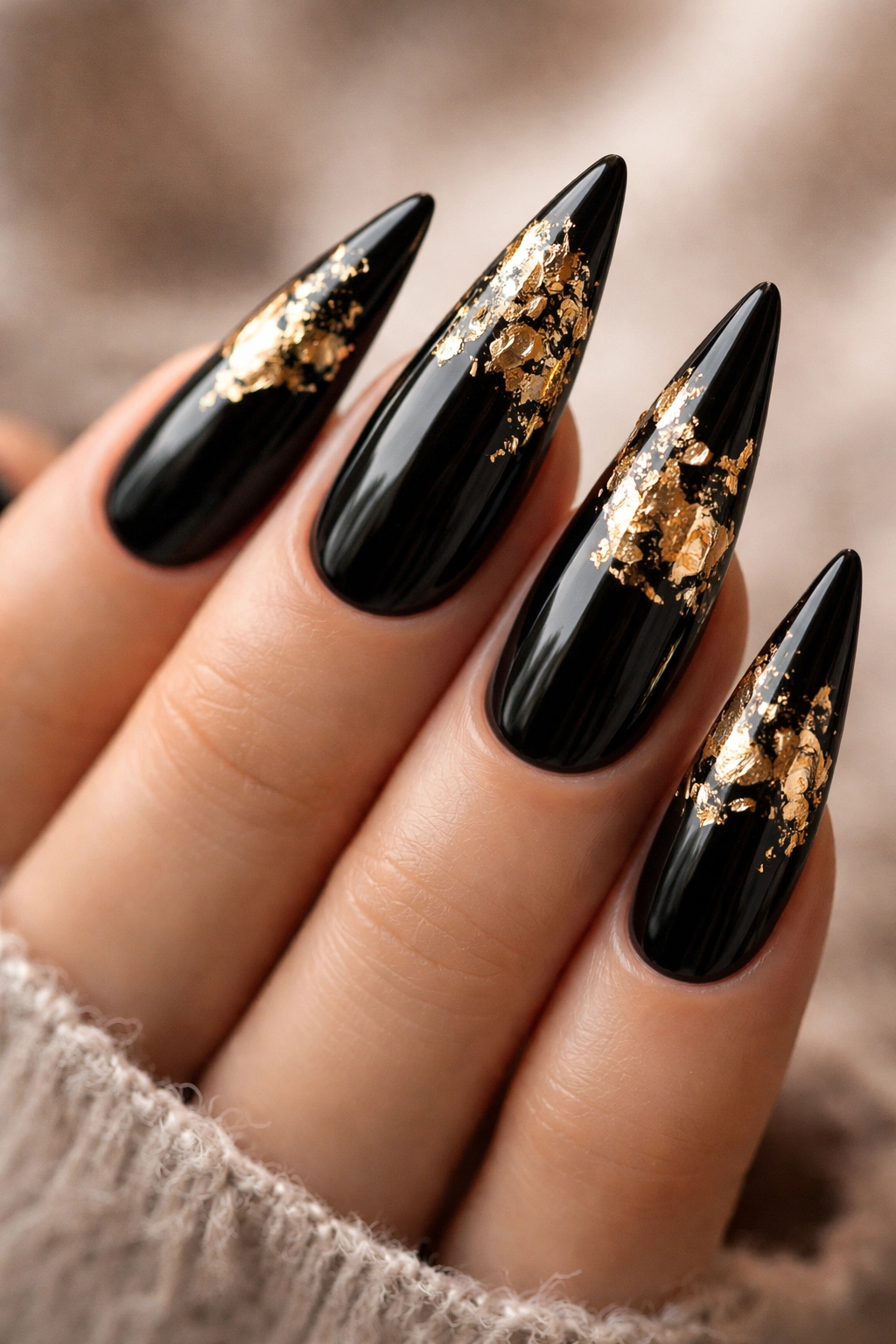 Close-up of black stiletto nails with gold leaf accents.