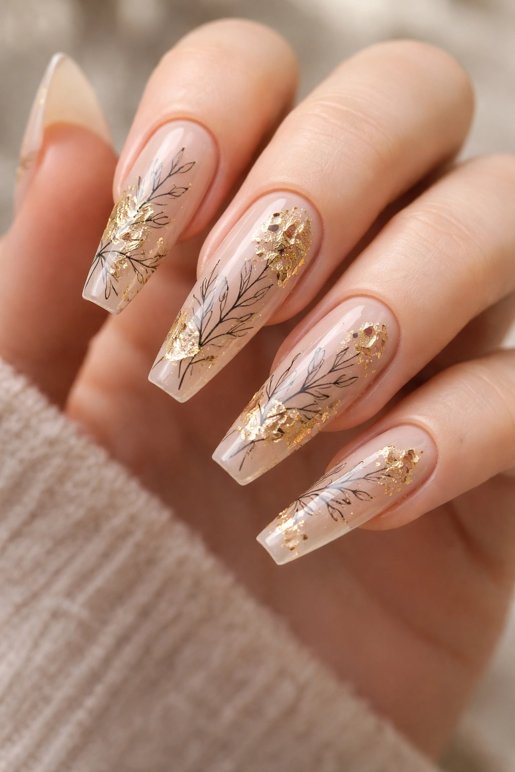 Close-up of long coffin nails with gold leaf accents and botanical art
