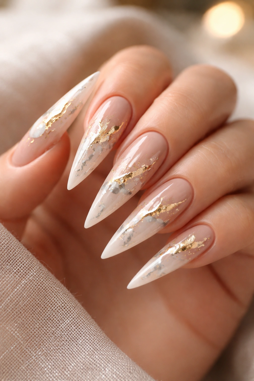 Stiletto nails with nude base, gold leaf, and marble veining.