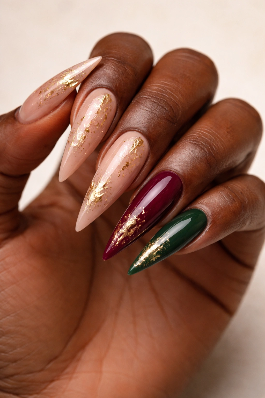 Nude base nails with gold leaf accents and accent nails in burgundy and green