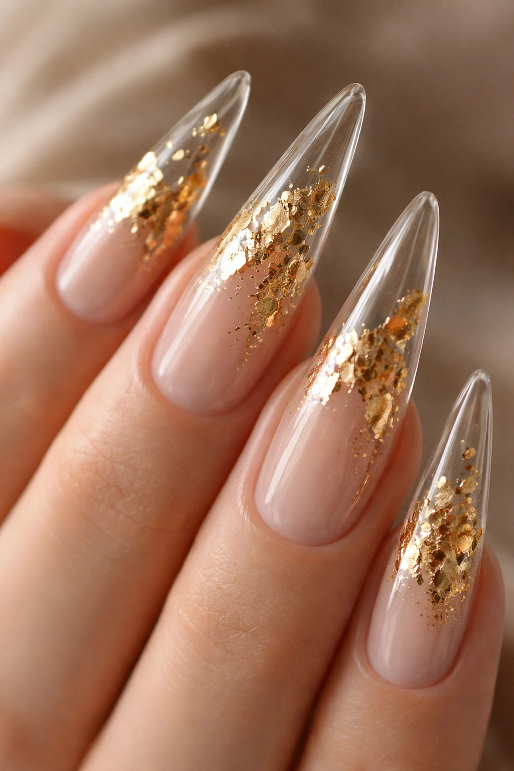 Clear stiletto nails with gold leaf accents reflecting light